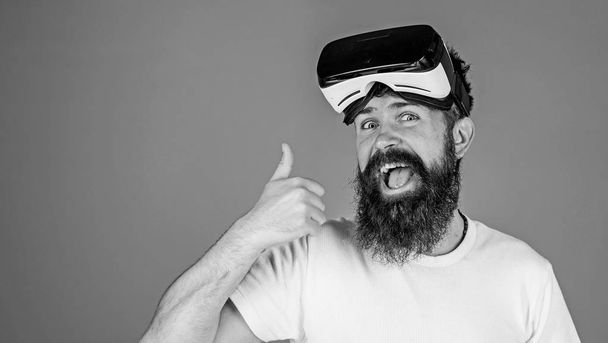 Man with long beard on happy face showing thumb up. Bearded man with excited look testing new model of VR headset, digital progress concept. Hipster with trendy beard isolated on blue background - Foto, afbeelding