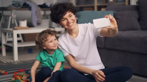 Young mother and little son taking selfie with smartphone camera in apartment - Πλάνα, βίντεο