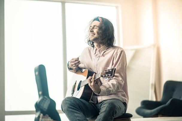 Cheerful handsome young guitarist sitting in bright room - 写真・画像