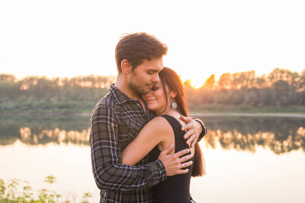 Concepto romántico y de personas - pareja joven abrazándose juntos cerca del río o del lago y disfrutando de la hora de verano
 - Foto, Imagen