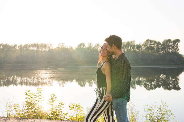Romantic and people concept - young couple hugging together near the river or lake and enjoying summer time - Фото, изображение