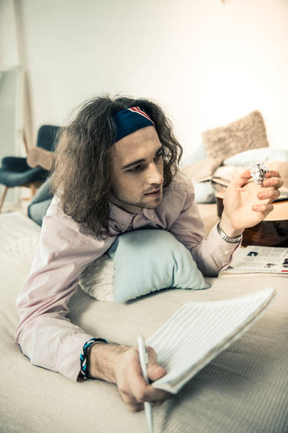 Dark-haired young musician squeezing piece of paper from his album - 写真・画像
