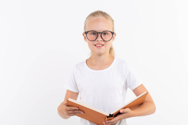oktatás, emberek, gyerekek és az iskolai koncepció - iskolai diák szemüveg könyvet tartja kezében a fehér háttér - Fotó, kép