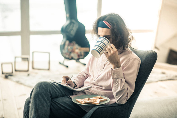 Hungry long-haired creator drinking tea from big cup - 写真・画像