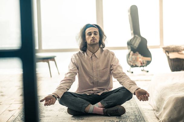 Peaceful long-haired man sitting in lotus posture in the middle of the room - Fotó, kép