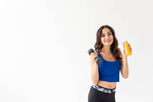 Sport, healthy lifestyle, people concept - young woman holds bottle of juice and a dumbbell on white background with copy space - Photo, Image