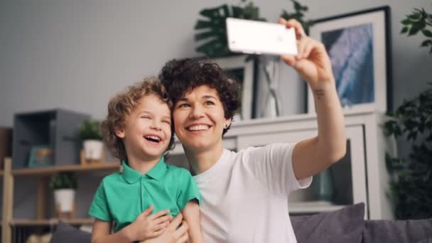 Pretty girl taking selfie with cute son laughing having fun holding smartphone - Záběry, video