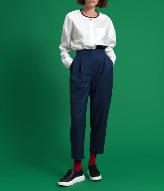 A girl with red hair in a beautiful, fashionable, luxurious white shirt and blue trousers, on a green background - Photo, image