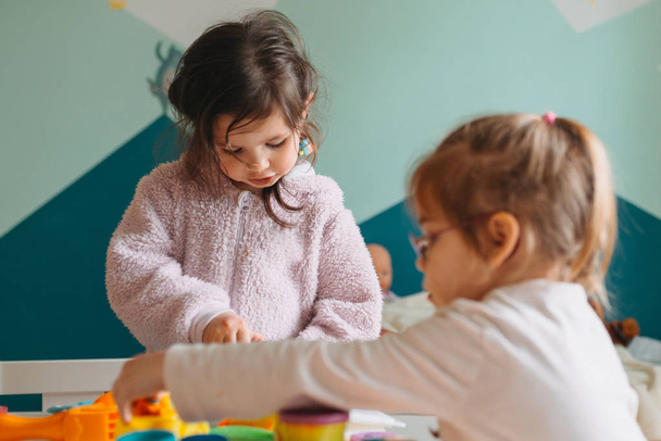 two little girls play in nursery with play dough - Fotó, kép
