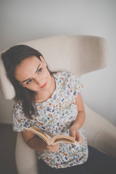 Cute young woman reading a book in a designer chair  - Fotó, kép