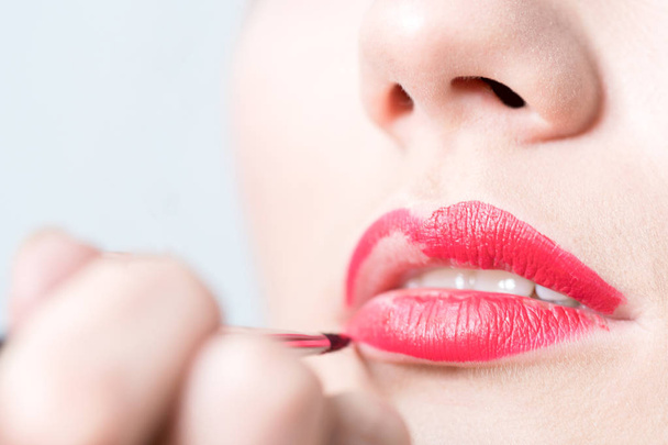 Closeup of girl paints lips with red lipstick - Valokuva, kuva