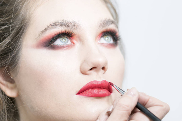 Makeup artist applies red lipstick. Beautiful female face. Sensual lips. Close-up - Foto, Imagem