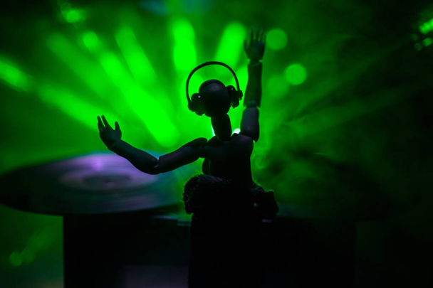 Dj club concept. Woman DJ mixing, and Scratching in a Night Club. Girl silhouette on dj's deck, strobe lights and fog on background. Creative artwork decoration with toy. Selective focus - Photo, Image