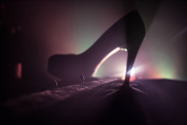 Decorazione d'arte. Silhouette di un uomo in piedi in mezzo alla strada in una notte nebbiosa con gigantesche scarpe da donna tacco alto. Potere delle donne o concetto di dominazione delle donne. Focus selettivo
 - Foto, immagini