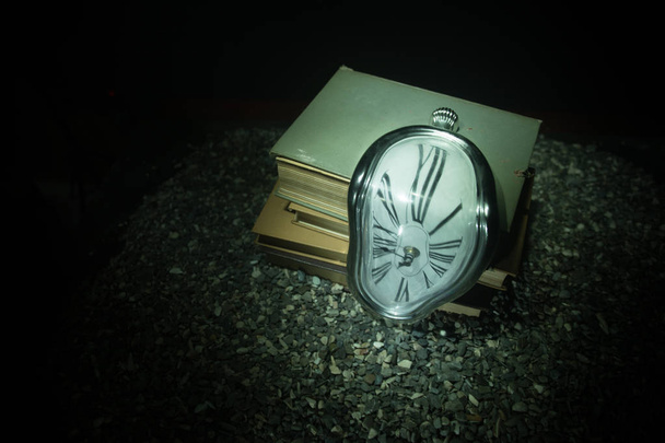 Έννοια του χρόνου. Παραμορφωμένη μαλακό τήξης ρολόι για τα παλιά βιβλία. Με σκοτεινά τονισμένα ομιχλώδες φόντο. Επιλεκτική εστίαση - Φωτογραφία, εικόνα