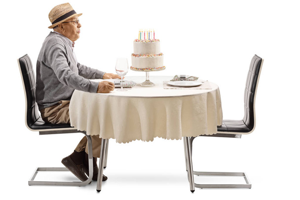 Excited senior man blowing candles on a cake at a restaurant table isolated on white background - Fotoğraf, Görsel