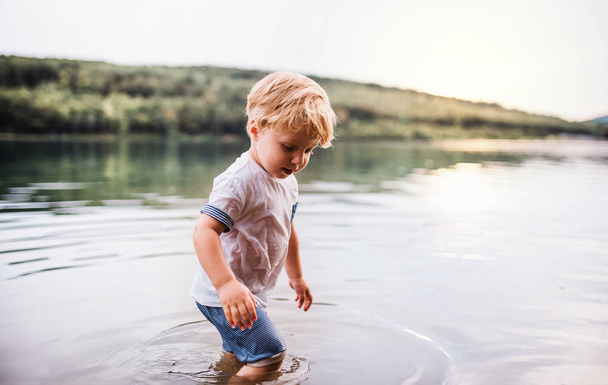ein nasser, kleiner Junge, der im Sommer draußen in einem Fluss spaziert und spielt. - Foto, Bild