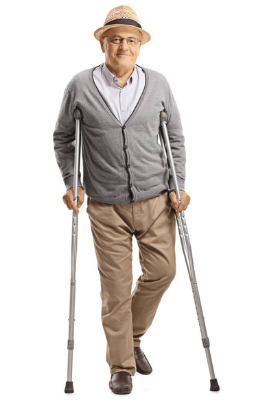 Full length portrait of a senior man walking with crutches and smiling at the camera isolated on white background - Foto, Imagen