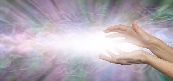 Енергетичні потоки, де йде ваша увага - паралельні жіночі руки з чудовим потоком білої енергії, що витікає на тьмяному рожево-зеленому сірому фоні з копіювальним простором
 - Фото, зображення