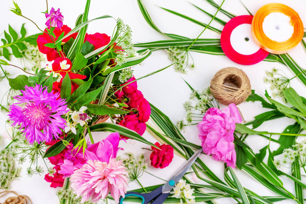 Flower composition with a bouquet of pink peony flowers, cornflowers and red roses and colored ribbons on a white background, top view flat lay - Foto, afbeelding