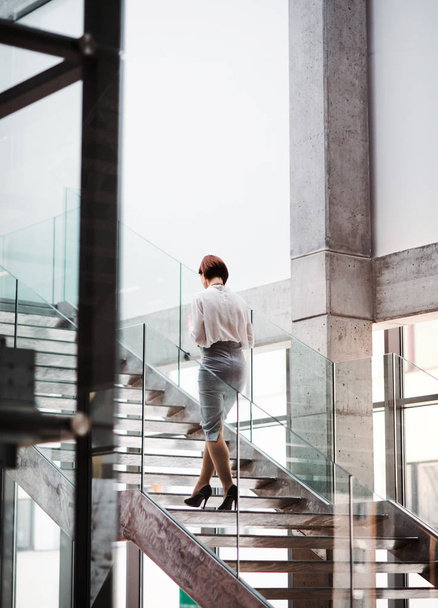 A rear view of young businesswoman walking up the stairs in office building. - Fotó, kép