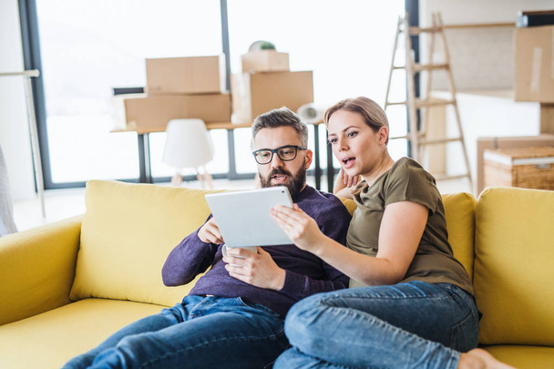 A young couple with tablet sitting on sofa, moving in new home. - Foto, Bild