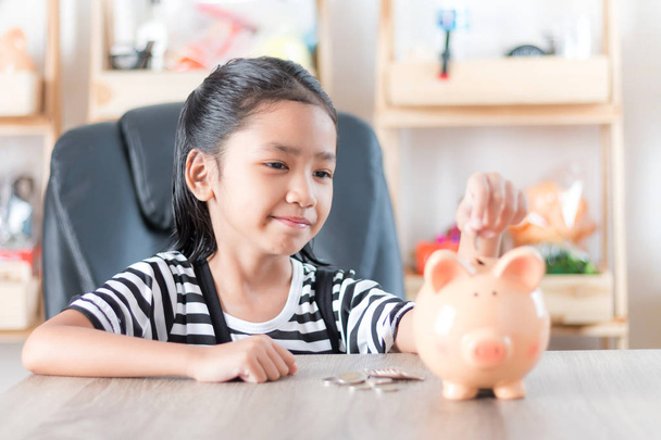 Asian little girl in putting coin in to piggy bank shallow depth - Zdjęcie, obraz