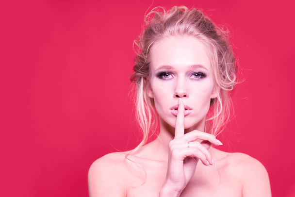 Secret. Cute girl with beautiful makeup and bare shoulders, presses her index finger to her lips on a red background - Фото, изображение