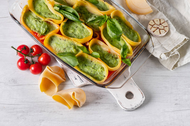 Traditionelle italienische gefüllte Lumaconi mit grüner Pesto-Sauce, serviert mit Tomaten und grünen Basilikumblättern - Foto, Bild