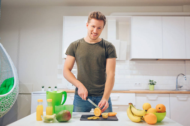 Young smiling man cooking fresh fruits in the kitchen. Healthy food. Vegetarian meal. Diet detox - Zdjęcie, obraz