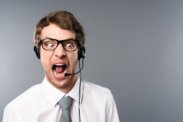 operador de call center irritado em fone de ouvido e óculos gritando em fundo cinza
 - Foto, Imagem
