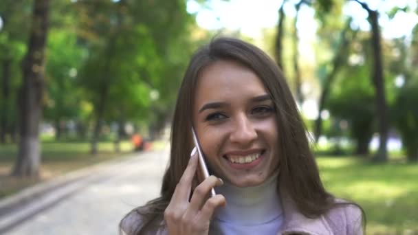   4k. Young smiling attractive  woman  talk by smartphone in sunny  city park .Steady shot - Filmagem, Vídeo