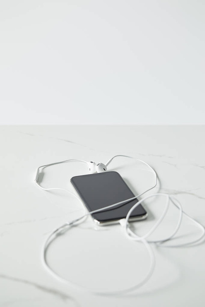 enfoque selectivo del smartphone con pantalla en blanco y auriculares aislados en gris
 - Foto, Imagen