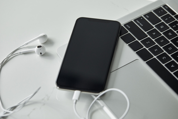 黒いキーボード、白い表面にブランク画面とイヤホンを備えたスマートフォン付きのラップトップ - 写真・画像