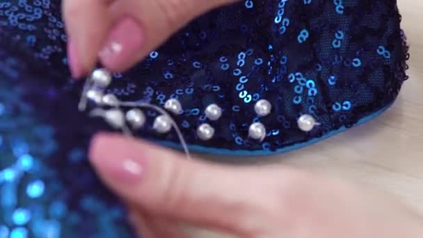 closeup rack focus of woman hands stitching beads to blue fabric with sequins - Filmati, video
