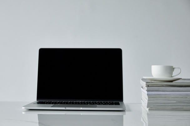 laptop with blank screen and coffee cup on stacked journals isolated on grey - Photo, Image