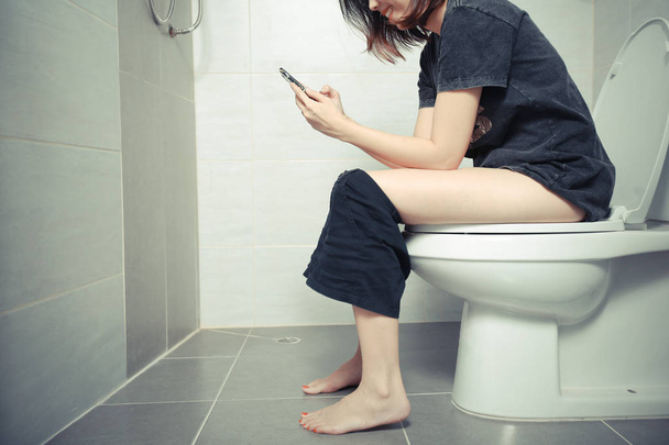 Femme utilisant un smartphone sur les toilettes le matin
. - Photo, image