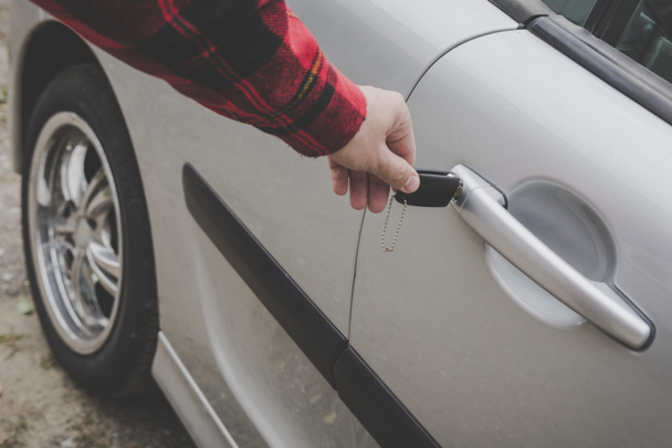 Closeup ενός ανθρώπου χέρι εισάγοντας ένα κλειδί σε το κλείδωμα πόρτα ενός αυτοκινήτου. Αγνώριστος λευκό άνδρα ανοίγει πόρτα του οχήματος από το κλειδί. Αδιάφορα ντυμένος άνθρωπος κλειδώνει ή ξεκλειδώνει το αυτοκίνητο. Βραχίονα προτεταμένο - Φωτογραφία, εικόνα
