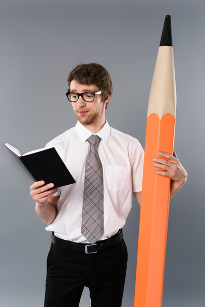 homme d'affaires concentré dans des lunettes tenant un énorme crayon décoratif et un livre de lecture sur fond gris
 - Photo, image