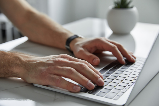 vista ritagliata dell'uomo utilizzando laptop con tastiera nera su tavolo in marmo bianco
 - Foto, immagini