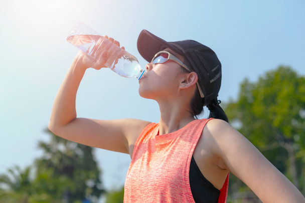 Beautiful fitness athlete woman drinking water after work out exercising on. evening summer. - Foto, immagini