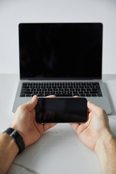 vista parcial de manos masculinas con smartphone y portátil con pantalla en blanco aislado en gris
 - Foto, imagen
