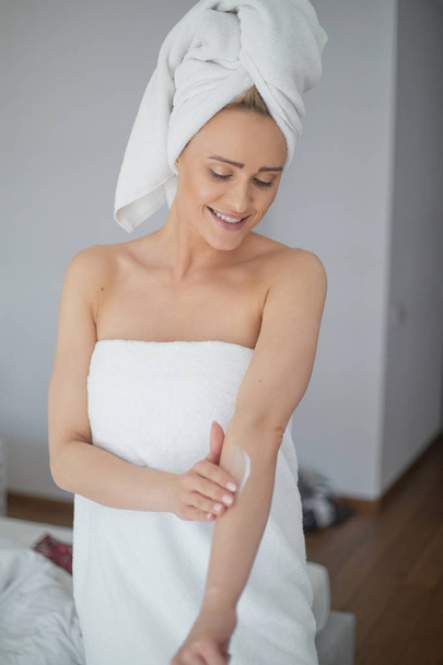 Middle aged beautiful blond woman moisturizes arm after the shower - Photo, Image