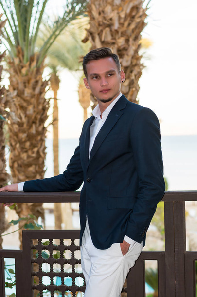 Young handsome man in a white shirt and suit stands on the balco - Foto, imagen