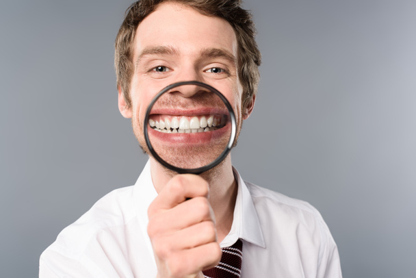 χαμογελώντας επιχειρηματία με τον μεγεθυντικό φακό σε γκρίζο φόντο - Φωτογραφία, εικόνα