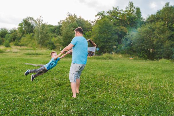 man spinning boy at green field. playing around - Fotó, kép