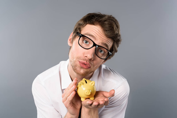 engraçado empresário em óculos segurando porquinho banco no fundo cinza
 - Foto, Imagem