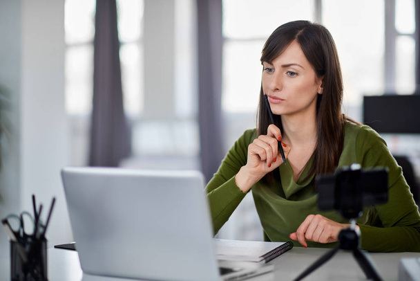 Beautiful serious Caucasian businesswoman sitting in modern office and using laptop. - Photo, image