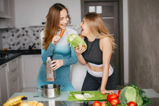 Two sports girl in a kitchen with vegetables - Fotoğraf, Görsel