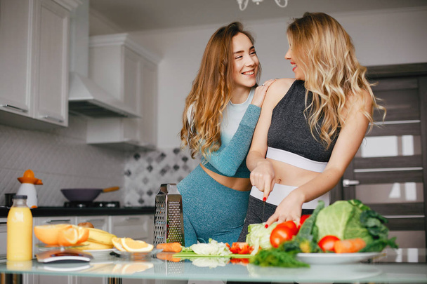Two sports girl in a kitchen with vegetables - Фото, изображение